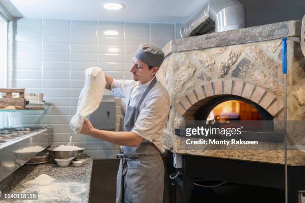 chef tossing and stretching the dough for pinsa romana, a roman style pizza blend reducing sugar and saturated fat, containing rice and soy with less gluten - pizza toss foto e immagini stock