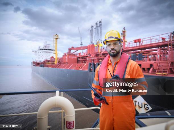 composite image of ship worker on tugboat with oil tanker - olietanker stockfoto's en -beelden