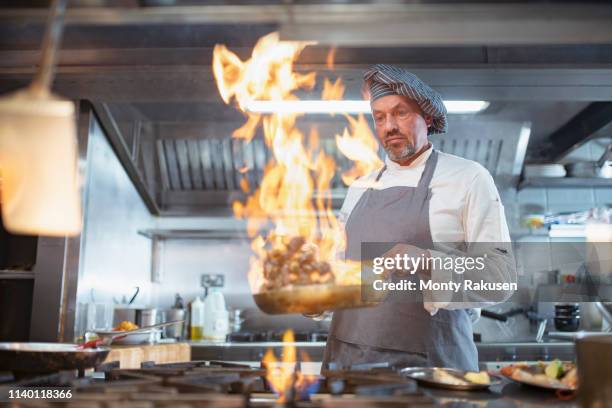 chef cooking with brandy (flambe) and flames in italian restaurant kitchen - extra portraits stockfoto's en -beelden