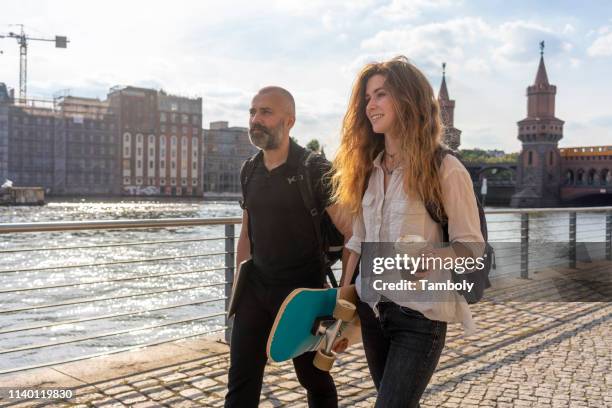 man and female friend with skateboard on bridge, river, oberbaum bridge and buildings in background, berlin, germany - advice woman travel traveling stock pictures, royalty-free photos & images