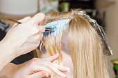 Hairdresser hands bleaching strands of blonde woman hair in beauty salon. Closeup.