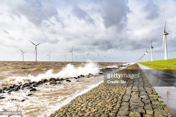 windturbines in een offshore windpark tijdens een storm met grote golven raken de wal - dyke stockfoto's en -beelden