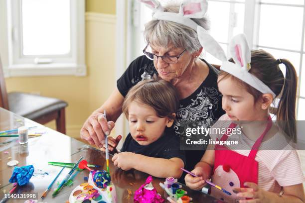 grandmother and sister and brother painting easter eggs - dirty easter stock pictures, royalty-free photos & images