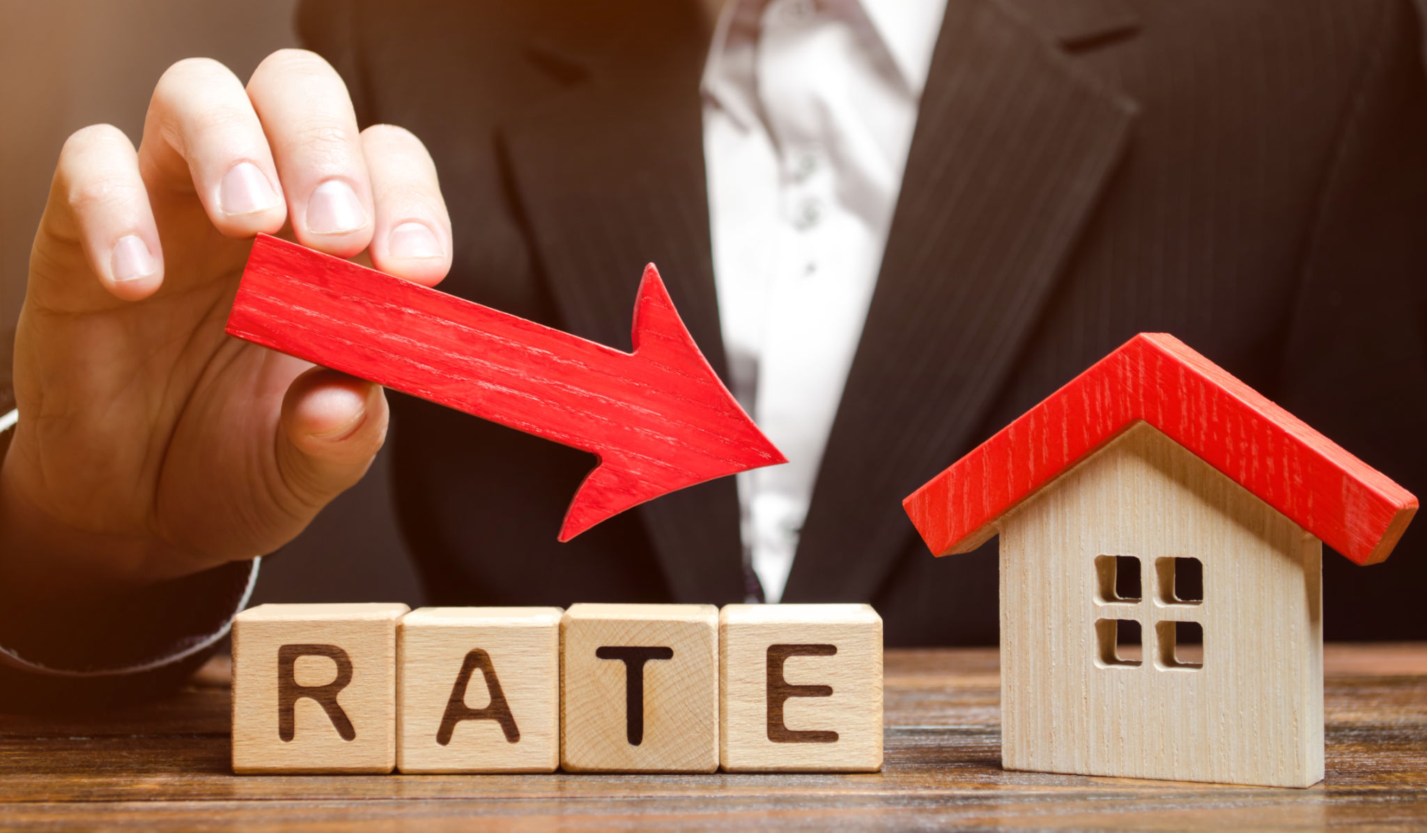 Businessman holding the down arrow on wooden blocks with the word Rate and house. Low interest in mortgages. Reducing interest payments for mortgage. The fall in housing rates on credit. Businessman holding the down arrow on wooden blocks with the word Rate and house. Low interest in mortgages. Reducing interest payments for mortgage. The fall in housing rates on credit.