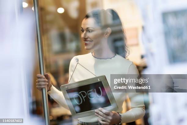 mature woman standing in shop , smiling, with open sign hanging in window - mode verkäuferin stock-fotos und bilder