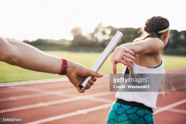 close-up of a athlete passing the baton to a female athlete - match sport stockfoto's en -beelden