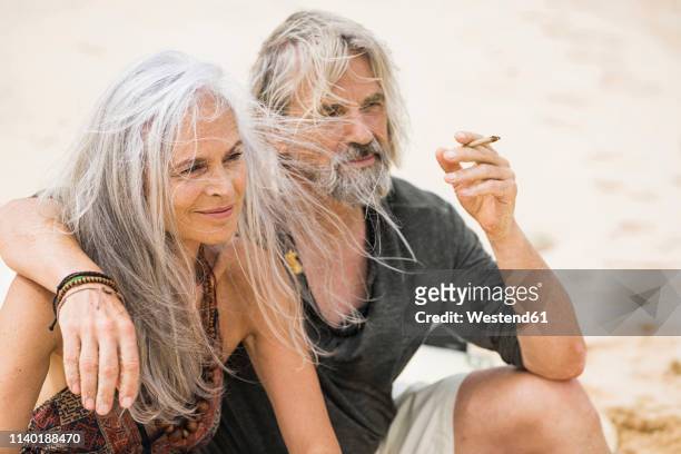 portrait of senior hippie couple smoking on the beach - long hair stock pictures, royalty-free photos & images