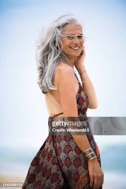 portrait of smiling senior hippie woman with sandy back on the beach - vrouw staat in mooie jurk stockfoto's en -beelden