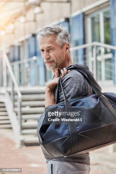 portrait of mature man with sports bag standing in front of gym - carrying sports bag foto e immagini stock
