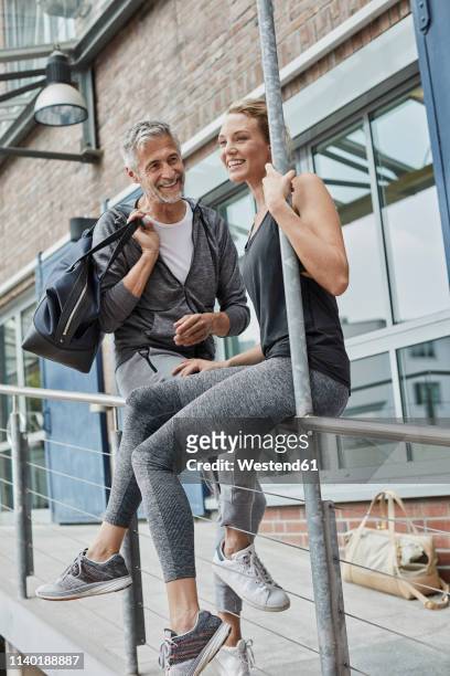 portrait of mature man with sports bag and laughing young woman in front of gym - flirting gym stock pictures, royalty-free photos & images
