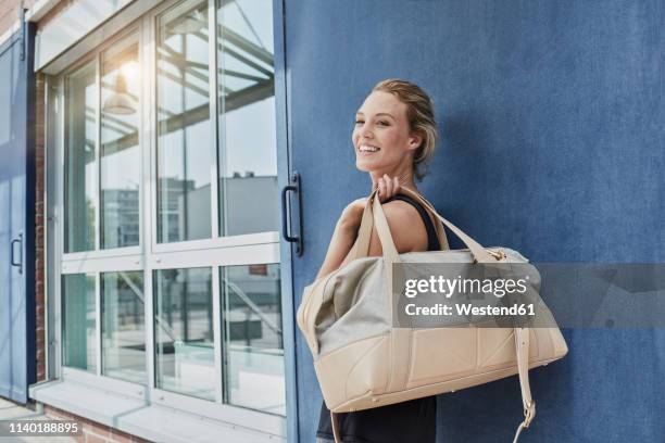 portrait of smiling young woman with sports bag in front of gym - woman gym stock-fotos und bilder