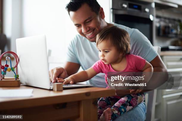 smiling father and baby girl using laptop on table at home - holding laptop stock pictures, royalty-free photos & images