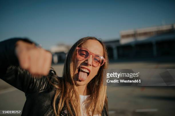 portrait of young woman outdoors sticking out tongue and punching - rebellion stock pictures, royalty-free photos & images
