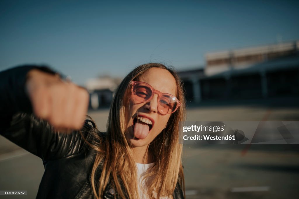 Portrait of young woman outdoors sticking out tongue and punching