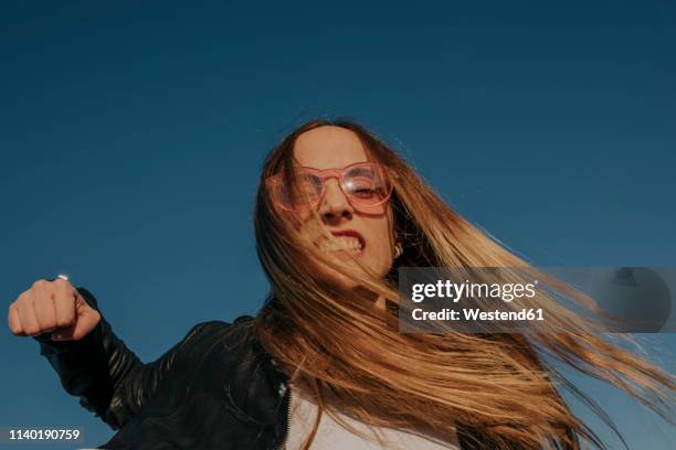 portrait of aggressive young woman punching under blue sky - rage stock pictures, royalty-free photos & images