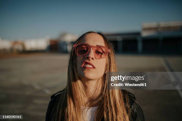 portrait of young woman with defiant attitude wearing sunglasses outdoors - arrogant stock-fotos und bilder