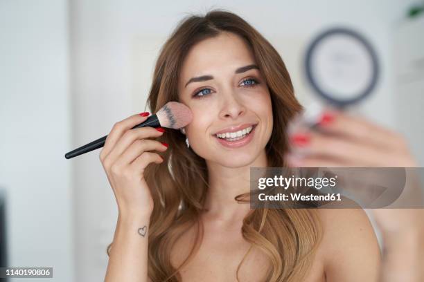 smiling young woman applying make-up - make up blush imagens e fotografias de stock