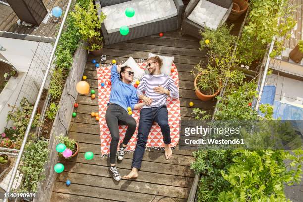 young couple relaxing on their balcony, lying on blanket with arms around - balkon stockfoto's en -beelden