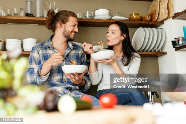 happy couple sitting in kitchen, eating spaghetti - the joys of eating spaghetti stock pictures, royalty-free photos & images