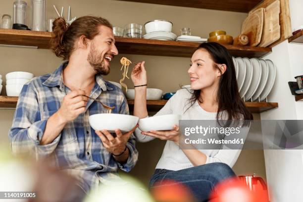 happy couple sitting in kitchen, eating spaghetti - couple eating foto e immagini stock