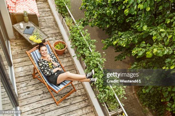 young woman sitting in deck chair, relaxing on her balcony - deck chair 個照片及圖片檔