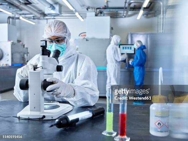 chemists working in industrial laboratory, wearing protective clothing, using microscope - labor chemie stock-fotos und bilder