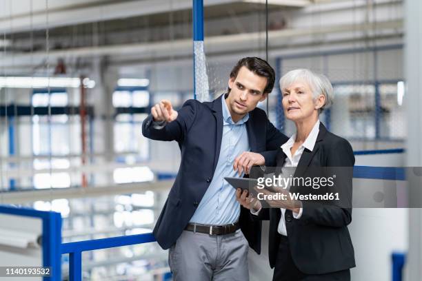 businessman and senior businesswoman with tablet talking in a factory - successor stockfoto's en -beelden