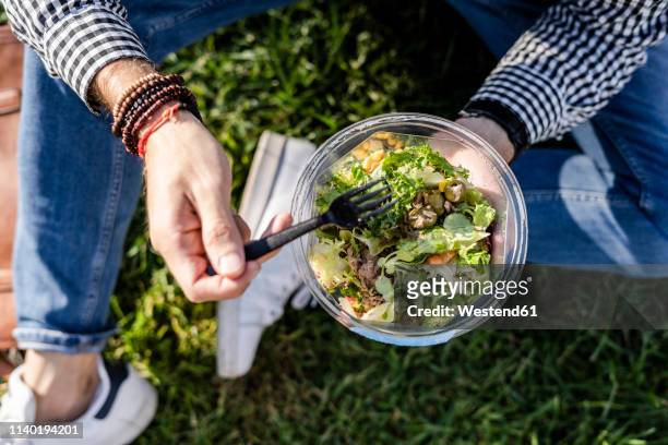 man sitting on a meadow eating mixed salad, partial view - eating salad stockfoto's en -beelden