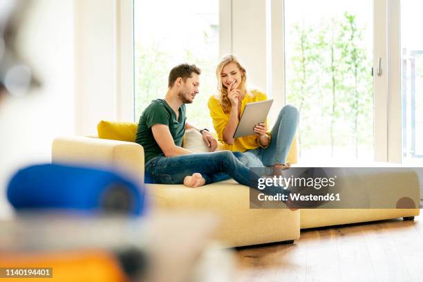 couple sitting on couch in their new home, using digital tablet - couple tablet stock-fotos und bilder