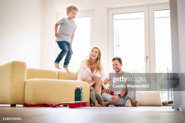 happy family moving into their new home, boy jumping on couch - jump dad stockfoto's en -beelden
