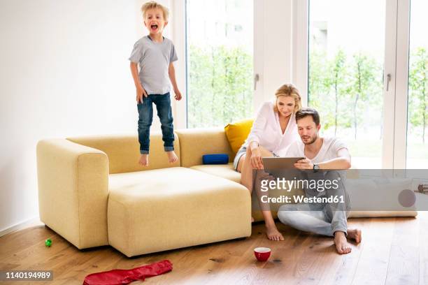 happy family moving into their new home, boy jumping on couch - gruppe springen ipad stock-fotos und bilder
