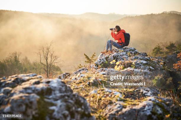 woman on a hiking trip in the mountains sitting on rock looking through binoculars - women wearing see through clothing stockfoto's en -beelden