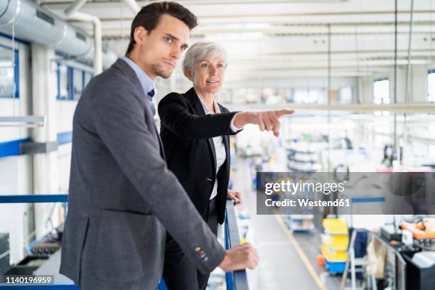 senior businesswoman and businessman on upper floor in factory overlooking shop floor - kontinuität stock-fotos und bilder