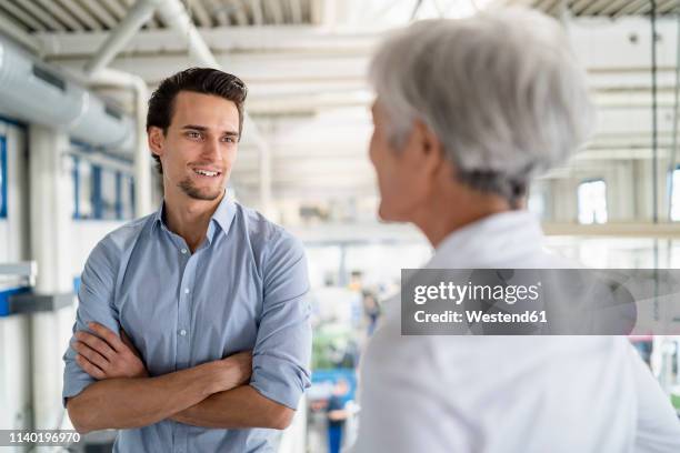 smiling businessman talking to senior businesswoman in a factory - business continuity stock-fotos und bilder