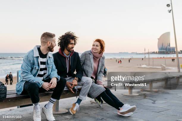 three happy friends sitting on a bench at the sea - promenade stockfoto's en -beelden