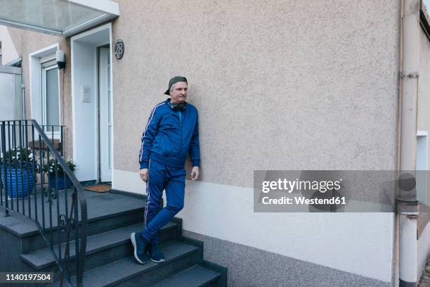 sportive senior man in tracksuit leaning against house wall - tracksuit fotografías e imágenes de stock