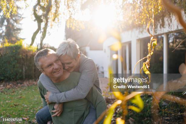 happy senior man carrying wife piggyback in garden - best ager paar garten stock-fotos und bilder