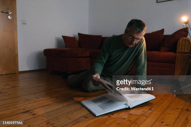 senior man sitting on the floor at home looking at photo album - looking to the past stock pictures, royalty-free photos & images