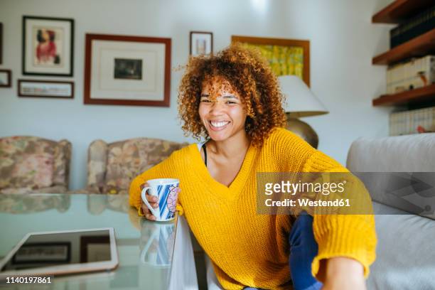 portrait of happy young woman with curly hair holding mug at home - anelzinho - fotografias e filmes do acervo