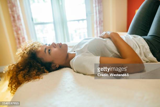 thoughtful young woman with curly hair lying in bed at home - auf dem rücken liegen stock-fotos und bilder