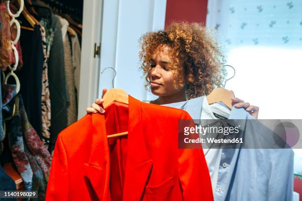 young woman with curly hair at home looking at clothing in her wardrobe - kiezen stockfoto's en -beelden