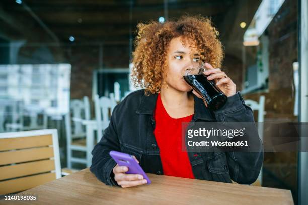 young woman with cell phone drinking cola at a bar - coca cola stock-fotos und bilder