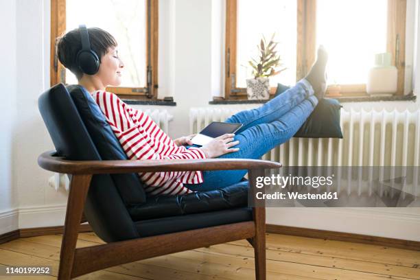 short-haired woman with headphones relaxing in lounge chair in stylish apartment - donna poltrona foto e immagini stock