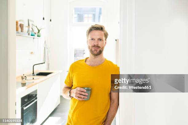 confident casual man with coffee mug leaning against door case - cup portraits foto e immagini stock