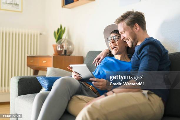 happy casual couple relaxing on couch using tablet and laughing - salon bleu photos et images de collection