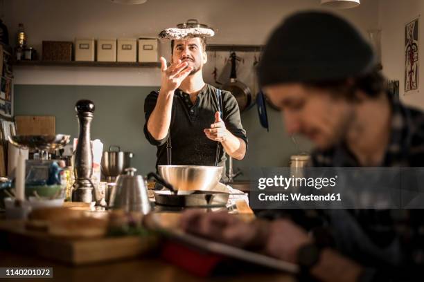 one man preparing bread dough while the other is using his digital tablet - hipster in a kitchen stockfoto's en -beelden