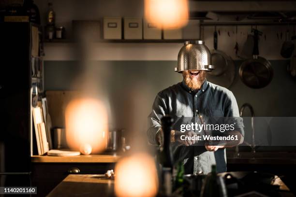 man sharpening kitchen, wearing colander as helmet - scherp stockfoto's en -beelden