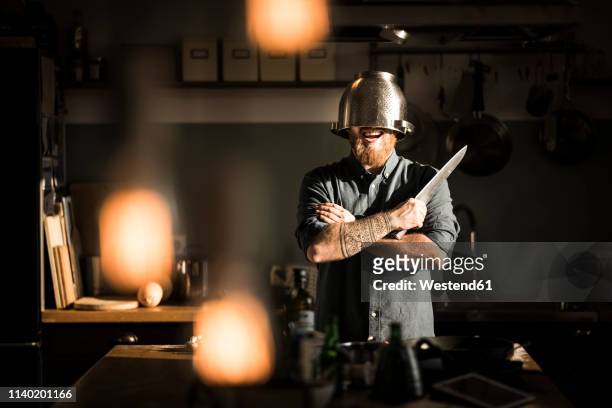 man with kitchen knife standing in kitchen, wearing colander as helmet - kitchen knife stockfoto's en -beelden
