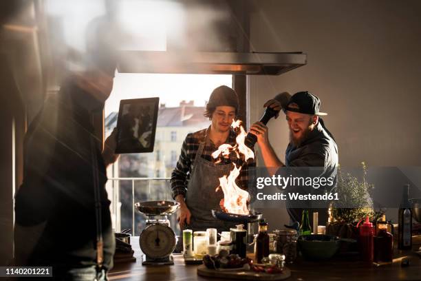 friends flambeing food in a pan, producing a big flame, while friend is filming - passion foto e immagini stock