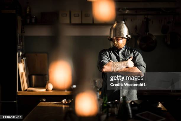 man standing in kitchen, wearing colander as helmet - colander foto e immagini stock